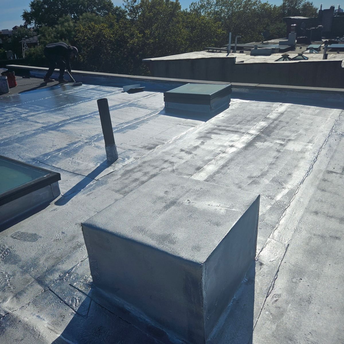 Worker applying protective coating on a flat roof to improve waterproofing and durability.