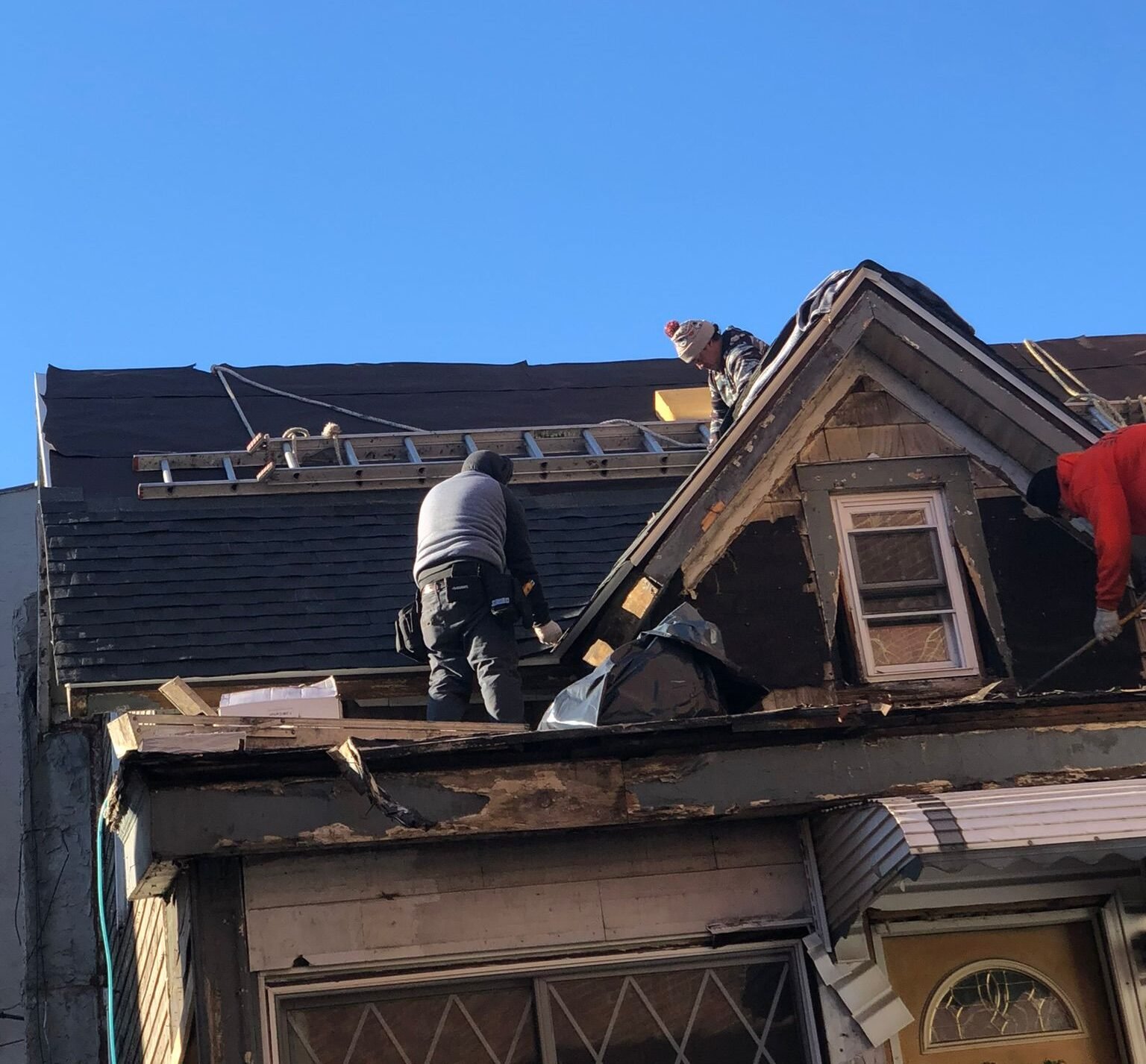 Two workers repairing the roof of a residential house by removing old shingles and fixing damaged areas.
