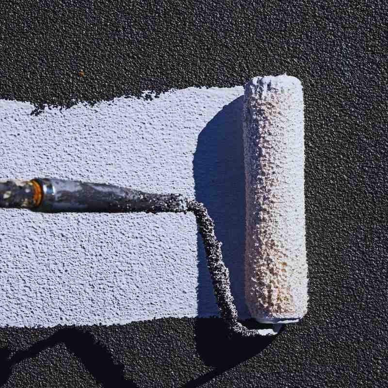 Close-up of roller applying white elastomeric coating on a flat roof surface.