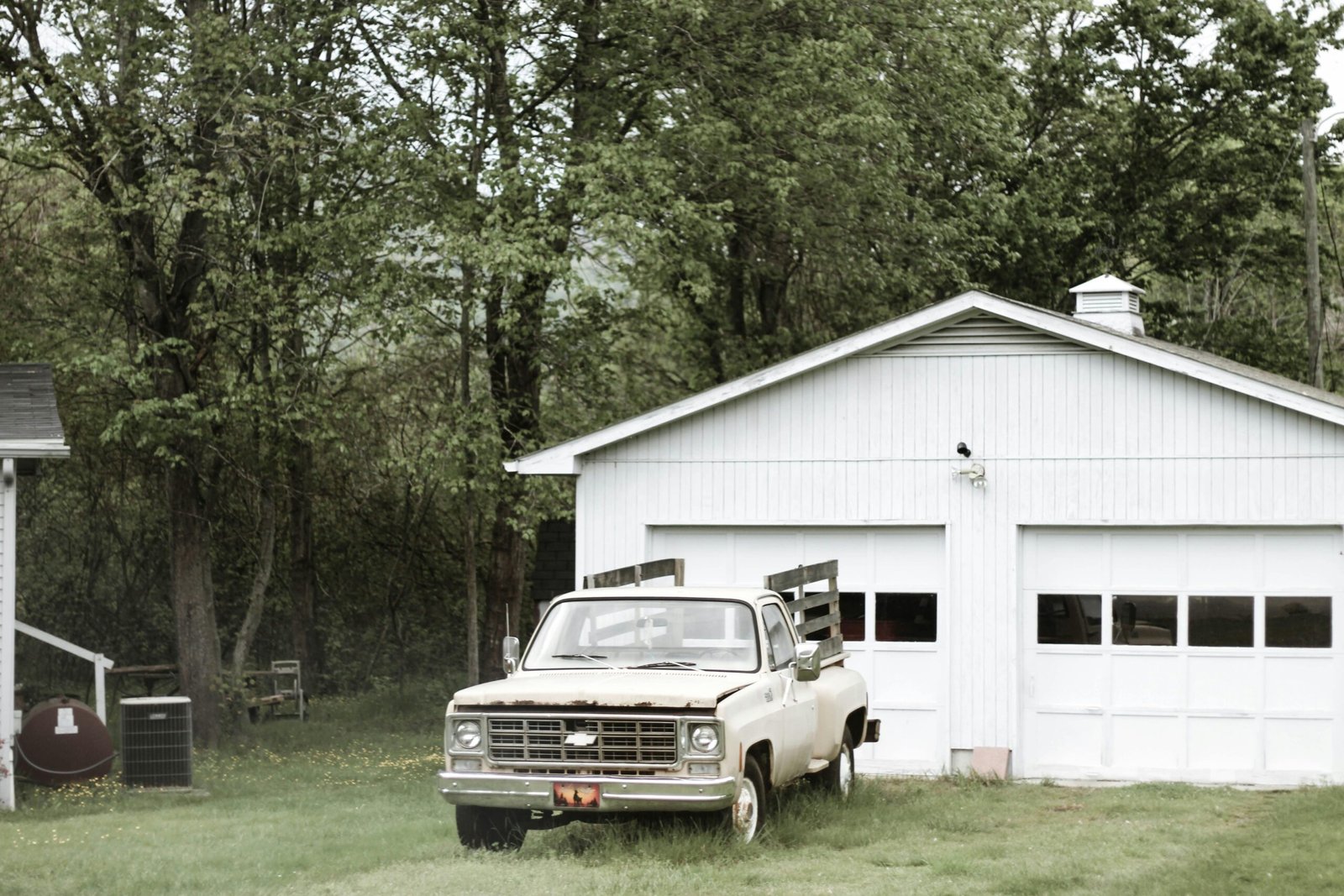 White wooden garage with double doors and an old pickup truck parked in front.