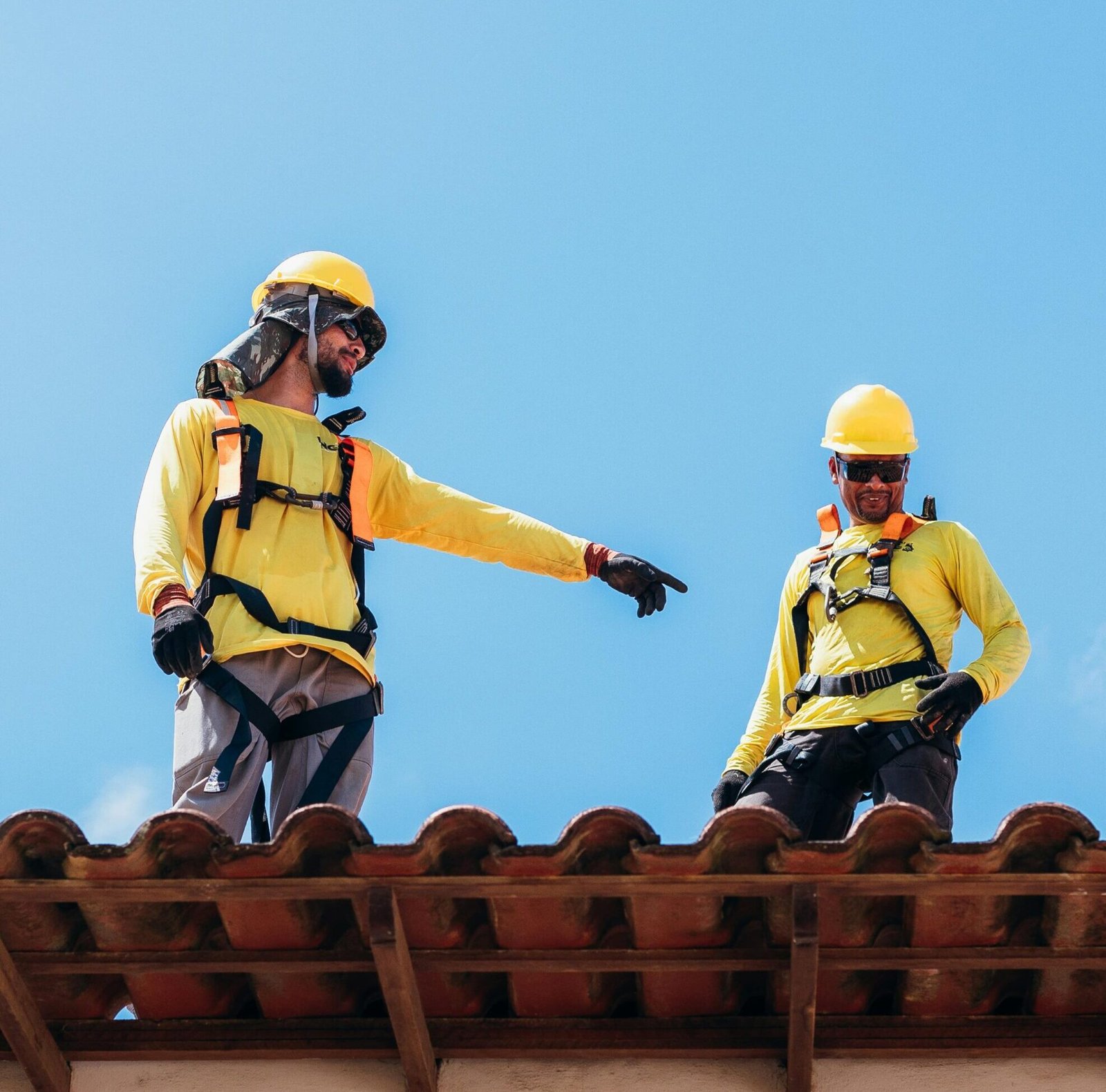 Two roofers wearing safety gear inspecting and discussing emergency roof repair on a tiled roof