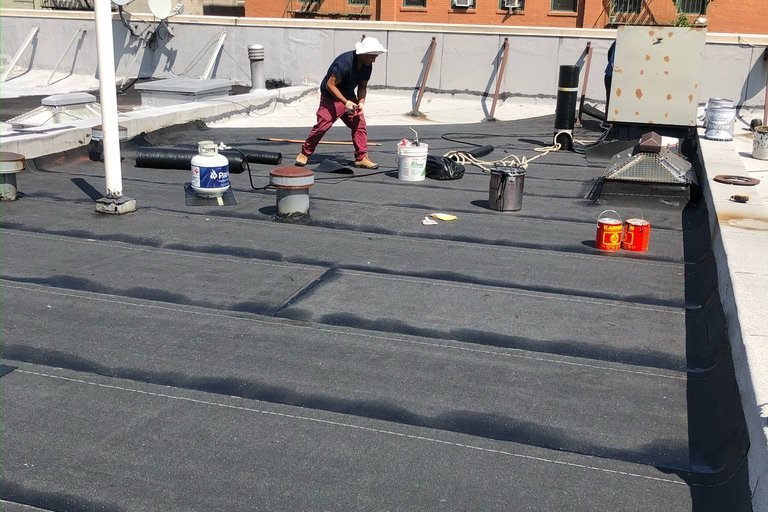 Roofer installing flat roof membrane on a NYC building